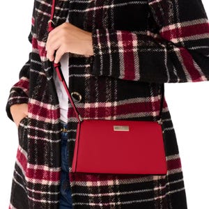 A red Kate Spade mini crossbody bag with a sleek rectangular shape, a thin adjustable shoulder strap, and a metal logo plate on the front.