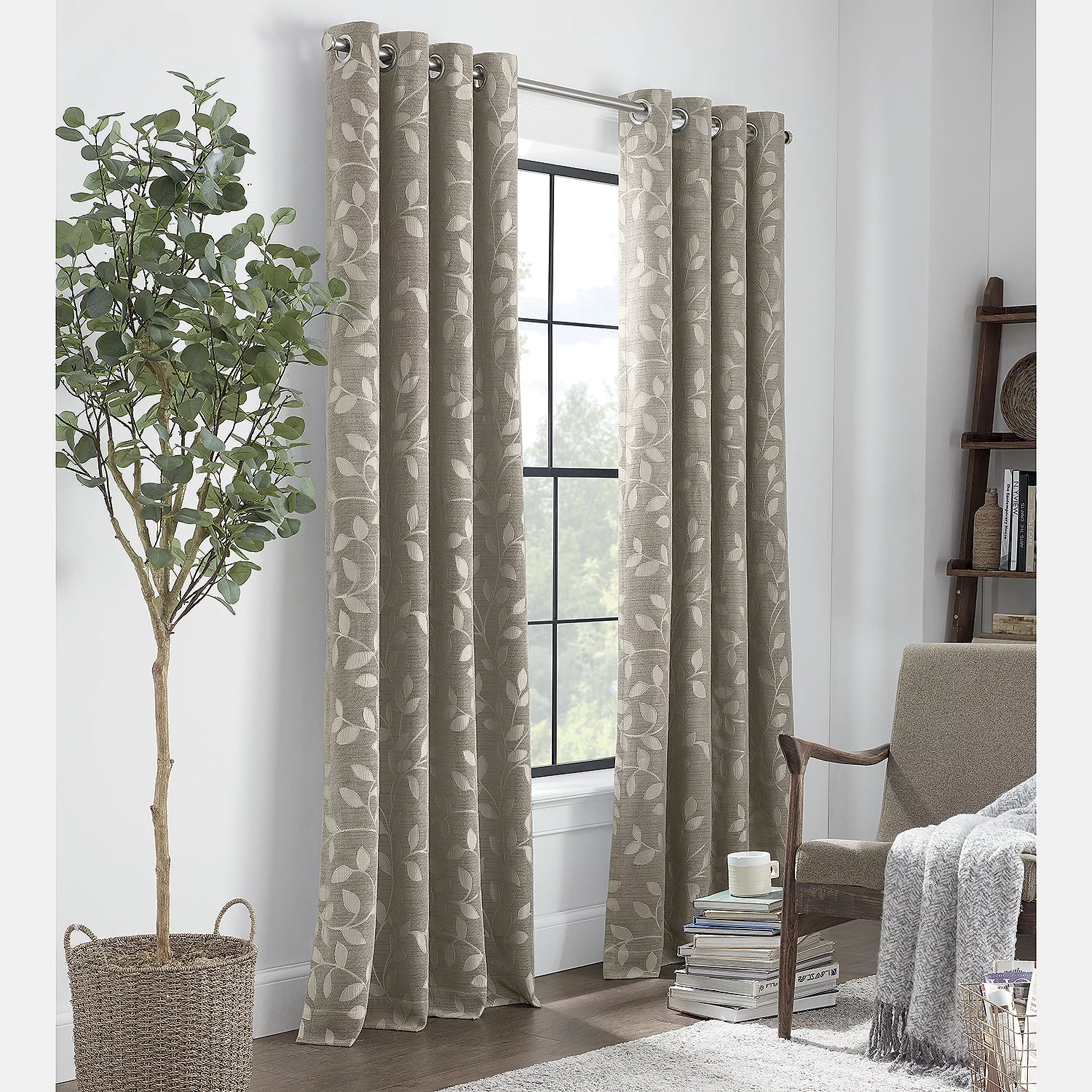 Patterned curtains hanging by a window, with a potted indoor tree and a wooden armchair draped with a grey throw beside it.