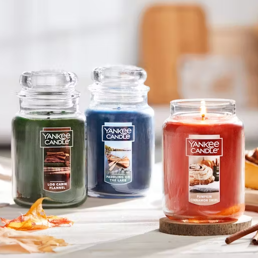 Three scented candles by Yankee Candle with labeled fragrances: Log Cabin Flannel, Paddling on the Lake, and Pumpkin Cinnamon Swirl, one of which is lit.