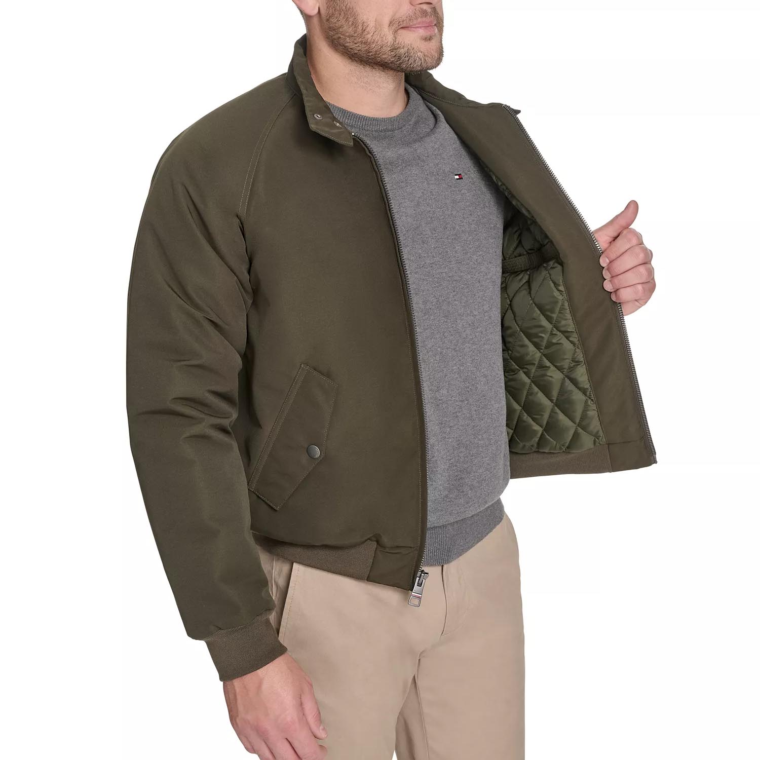 A man wearing a green bomber jacket with a quilted inner lining, over a gray sweatshirt, paired with beige pants.