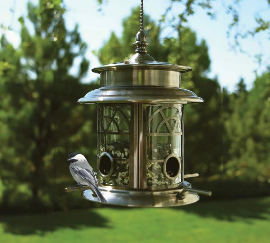 A bird feeder with a metal design hanging from a chain and a chickadee perched on it.