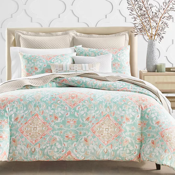 A patterned bedding set with complementary pillows and a vase with branches on a bedside table.