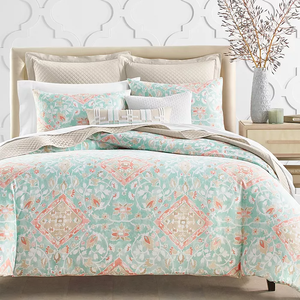 A patterned bedding set with complementary pillows and a vase with branches on a bedside table.