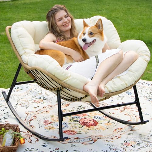 Woman sitting with a dog on a cozy cushioned rocking chair outdoors, placed on a decorative patterned rug.