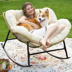 Woman sitting with a dog on a cozy cushioned rocking chair outdoors, placed on a decorative patterned rug.