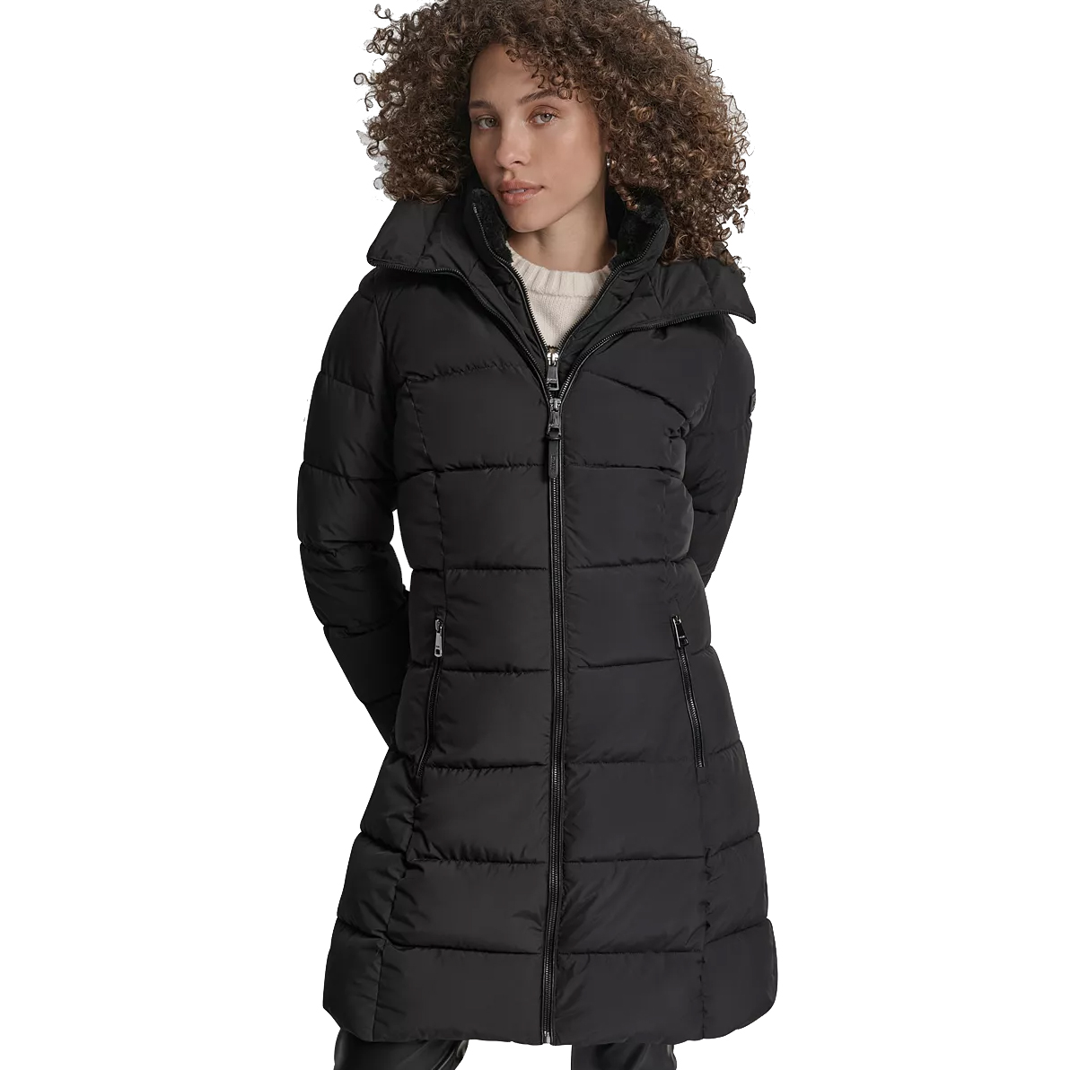 A woman is wearing a long black puffer coat with a front zipper, side pockets, and a high collar, over a light-colored sweater.