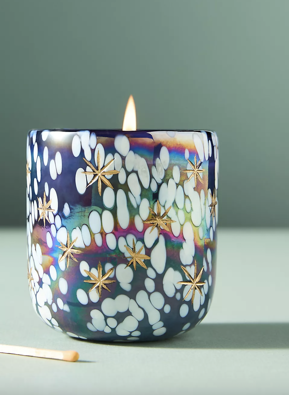 Decorative candle with a colorful, spotted glass holder featuring gold star designs.