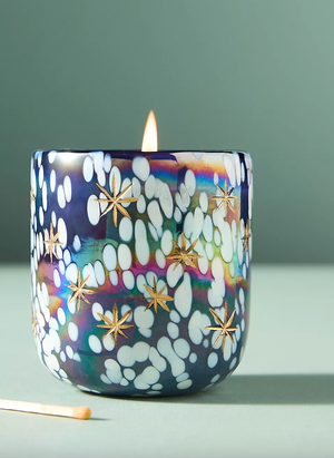 Decorative candle with a colorful, spotted glass holder featuring gold star designs.