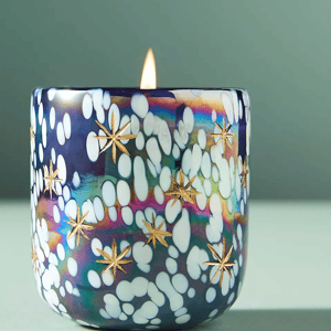 Decorative candle with a colorful, spotted glass holder featuring gold star designs.