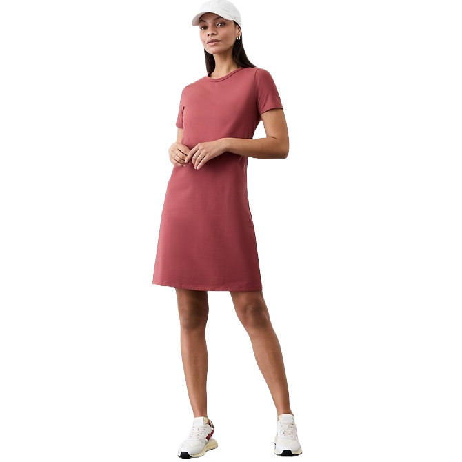A person is wearing a short-sleeve, knee-length pink dress with white sneakers and a white cap, displaying a casual outfit style.