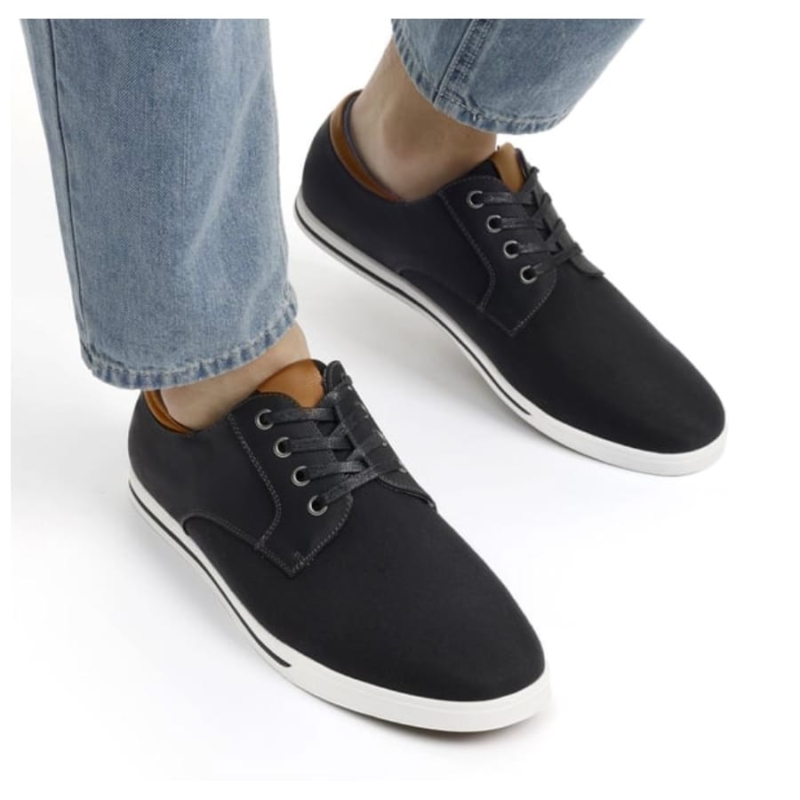 A pair of black sneakers with white soles, worn with rolled-up blue jeans.