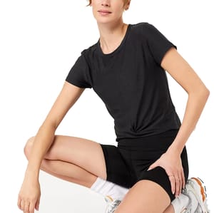 A model is wearing a black short-sleeved T-shirt paired with black athletic shorts and white socks with orange logo accents.