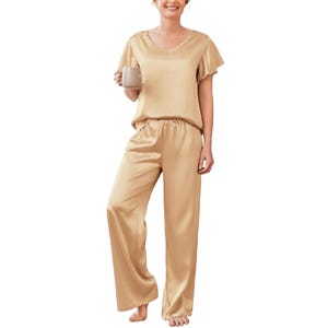 Women's satin pajama set featuring a short-sleeve V-neck top and long, loose-fitting pants in a beige color. The outfit has an elastic waistband for comfort.