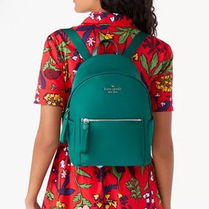 A woman wearing a floral dress is shown from the back, displaying a teal backpack with a zipper pocket.