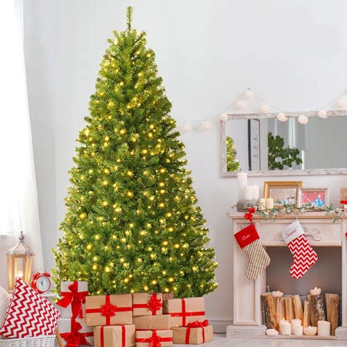 A decorated artificial Christmas tree with lights stands by a fireplace, surrounded by wrapped gifts and stocking decorations.