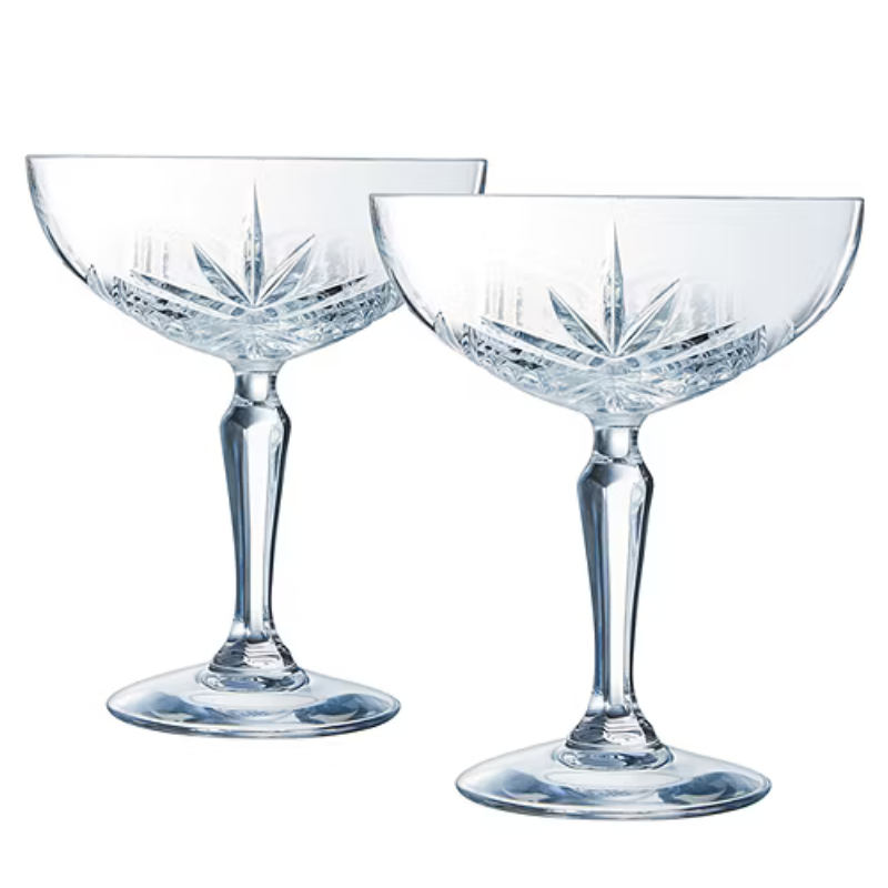 A pair of crystal champagne coupe glasses with intricate cut designs on the bowl, featuring long stems and wide bases.
