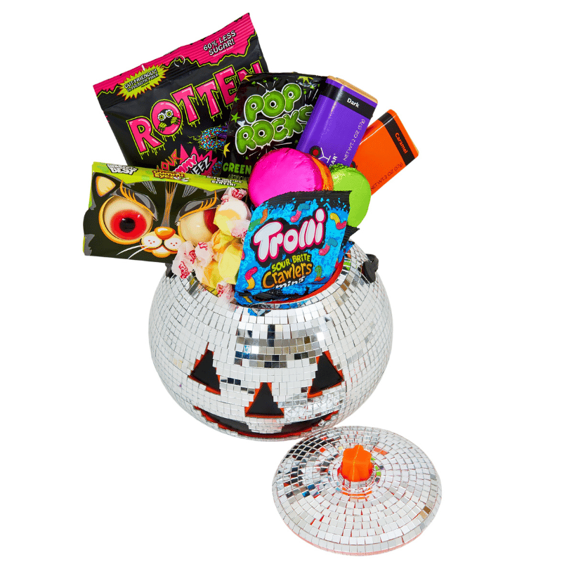 A mirrored pumpkin container filled with various candies, including Trolli Sour Brite Crawlers, Pop Rocks, Rotten gummies, and chocolate bars, with a lid featuring an orange knob.