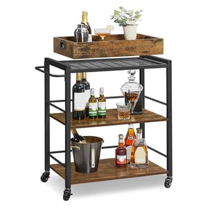 A rolling bar cart with three wooden shelves and a black metal frame holds various bottles, a decanter, ice bucket, and a serving tray with glasses and a potted plant on top.