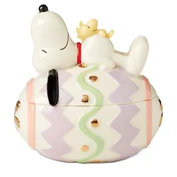 Ceramic container featuring a character lying on a pastel-colored egg with zigzag patterns and golden accents.