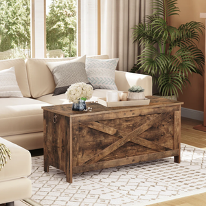 Living room featuring a beige sectional sofa, a rustic wooden chest-style coffee table with an \“X\“ pattern, a white patterned rug, decorative pillows, and a potted plant.