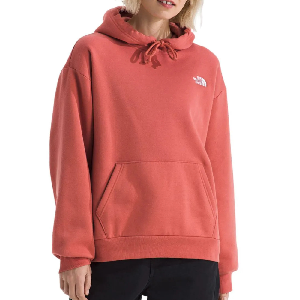A person wears a coral-colored The North Face hoodie featuring a drawstring hood, a kangaroo pocket, and a small logo on the left chest.