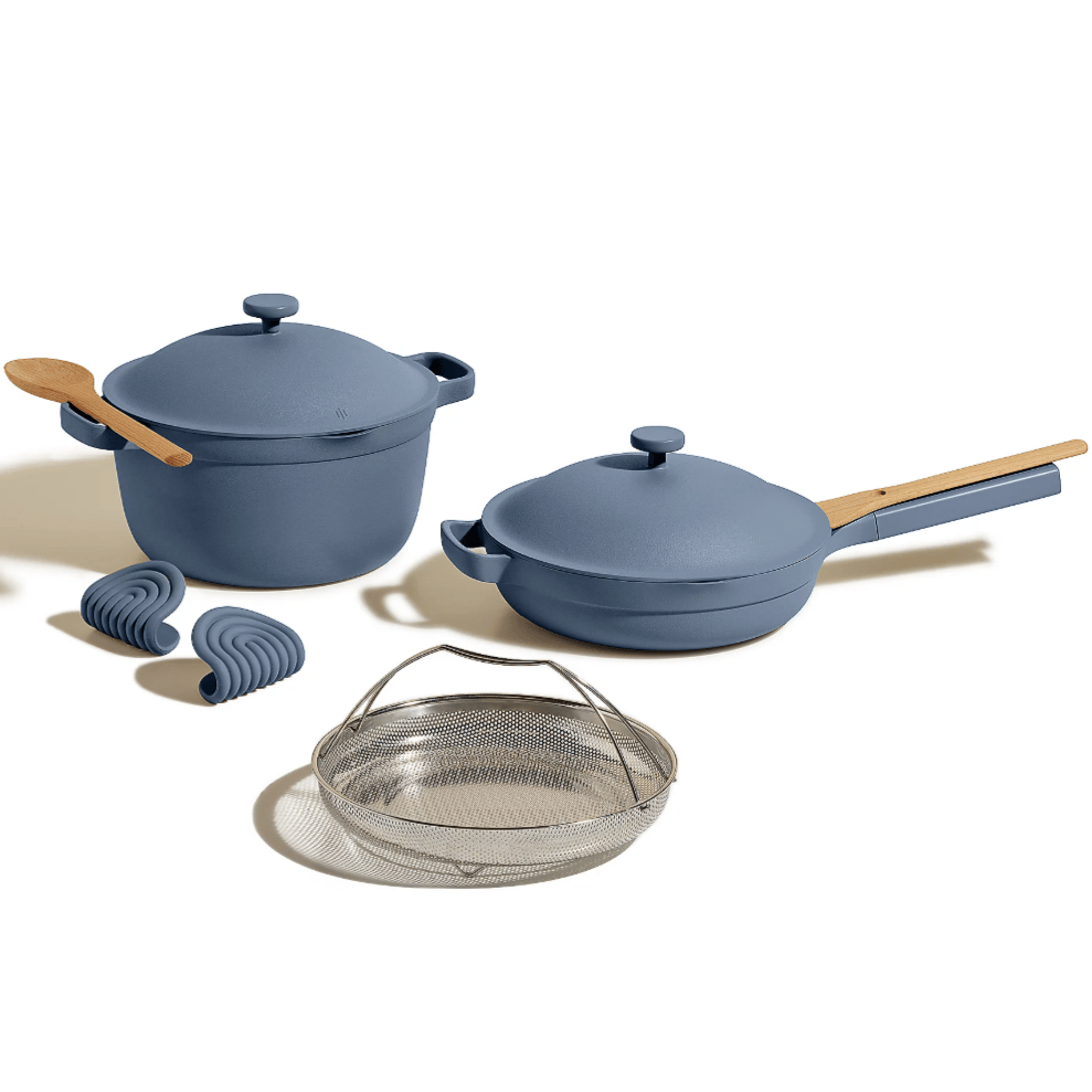A cookware set in blue includes a Dutch oven, a skillet with lid and wooden handles, a wooden spoon, two silicone grips, and a metal steamer basket.