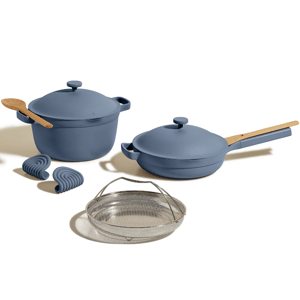 A cookware set in blue includes a Dutch oven, a skillet with lid and wooden handles, a wooden spoon, two silicone grips, and a metal steamer basket.