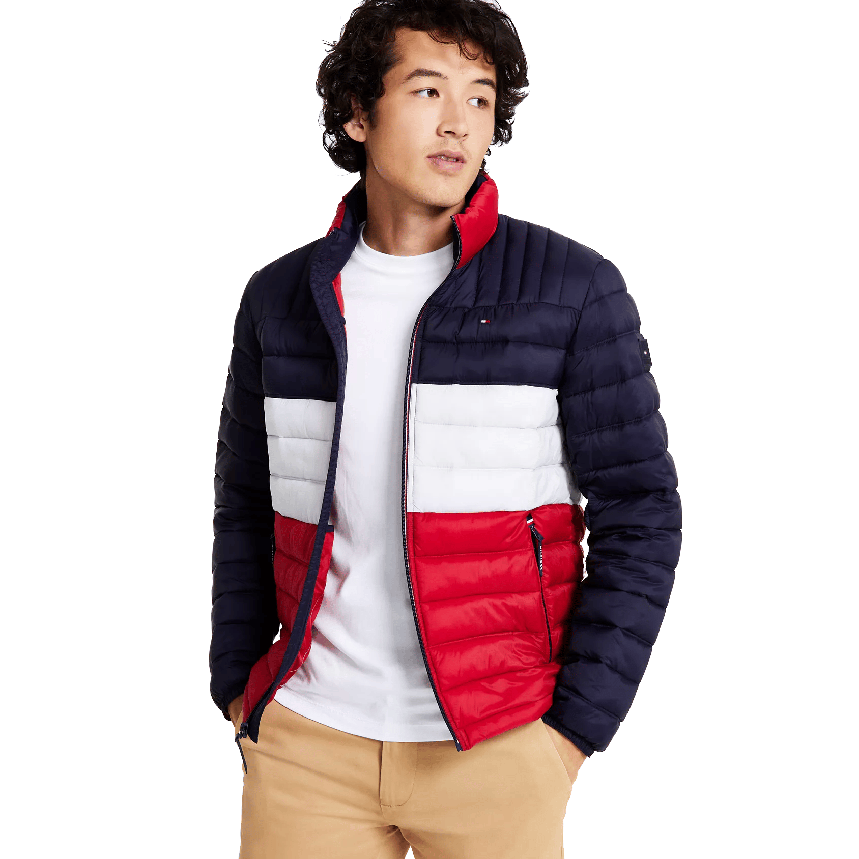 A man wearing a color-blocked puffer jacket with navy, white, and red sections paired with a white T-shirt and beige pants.