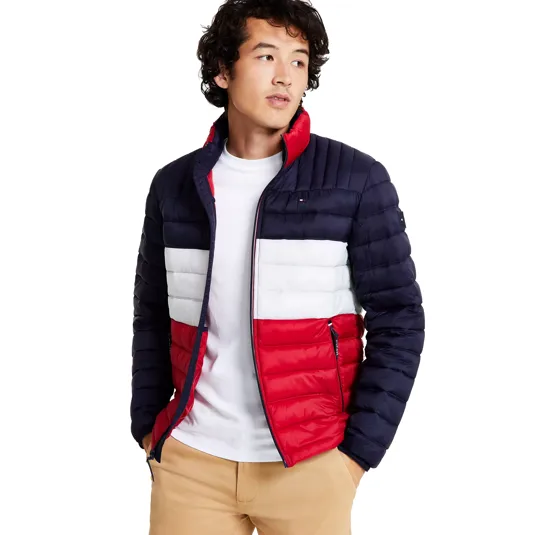 A man wearing a color-blocked puffer jacket with navy, white, and red sections paired with a white T-shirt and beige pants.