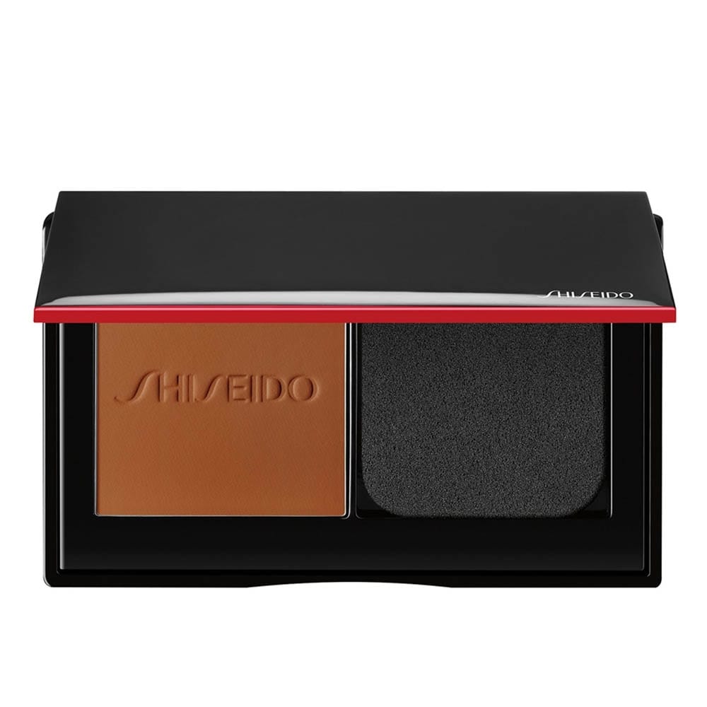 Shiseido powder foundation in a sleek black and red compact with the brand name embossed, featuring a warm-toned foundation pan and an adjacent black applicator sponge.