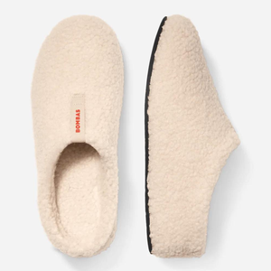 A pair of cream-colored sherpa slippers with a black sole and a visible 'BOMBAS' brand tag on the top.