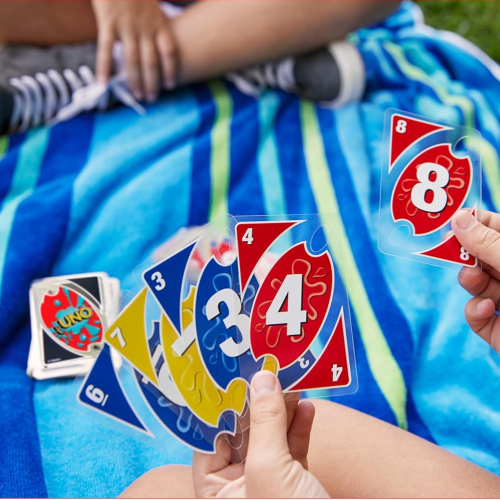 Water-resistant UNO cards on a striped towel with a person holding a hand of colorful, transparent cards.