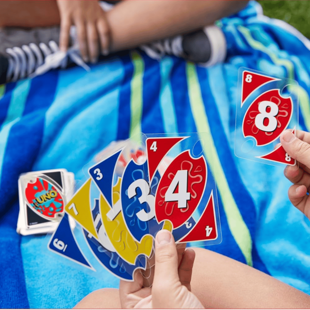 Water-resistant UNO cards on a striped towel with a person holding a hand of colorful, transparent cards.