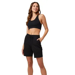 A woman in a black sports tank top and black shorts stands with her hand in the pocket.