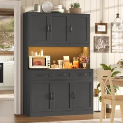 A dark wood kitchen cabinet with upper and lower storage features a countertop space displaying a small microwave, a cereal box, a clear jar, a pitcher, and a floral arrangement. Wall decor includes motivational signs, and there is dining furniture nearby.