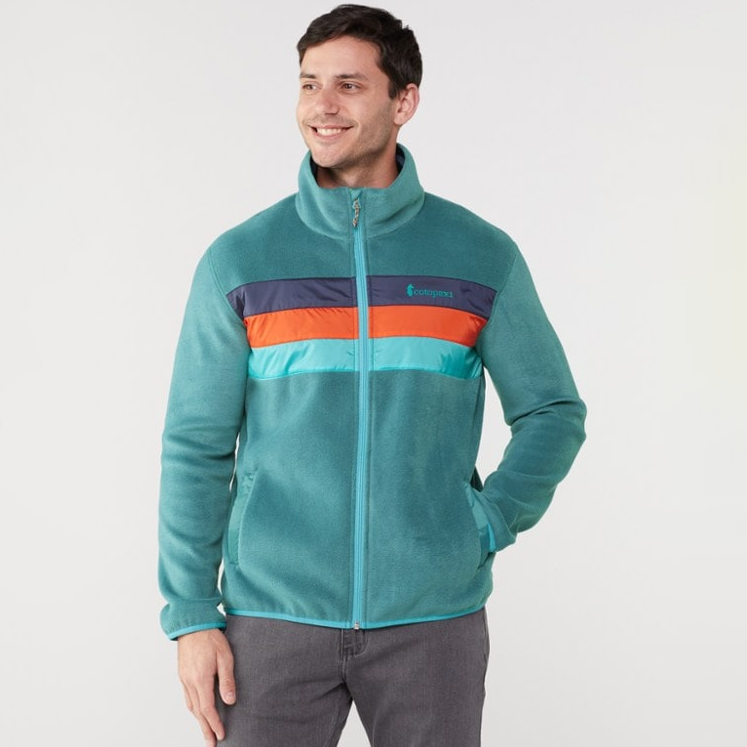 A man is wearing a teal fleece jacket with a horizontal striped panel featuring teal, orange, and blue colors, and there's a Cotopaxi logo on the chest.