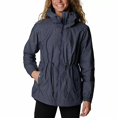 A woman is wearing the Columbia Lillian Ridge Jacket, which features a drawstring adjustable hood, a cinched waist, and buttoned side pockets.