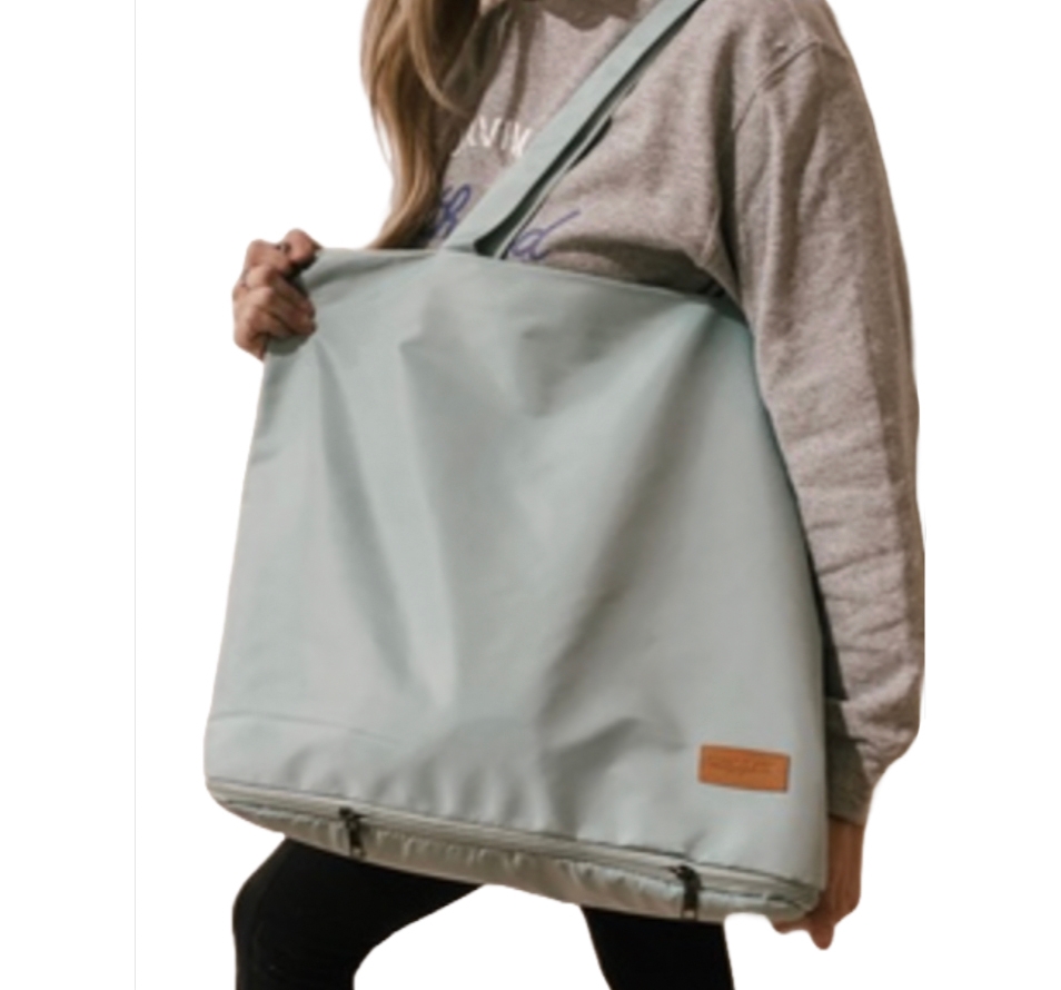 A person carrying a large, light blue tote bag with a shoulder strap and a small leather patch. The bag has a zipper at the bottom.