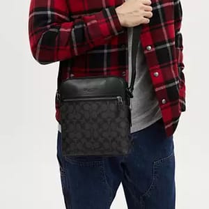 A person wearing a red and black plaid jacket with a gray shirt, blue jeans, and a black patterned crossbody bag.