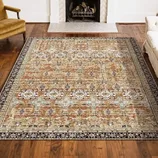 A patterned area rug with intricate floral and geometric designs, featuring a brown, beige, and black color scheme, placed on a wooden floor near a fireplace.