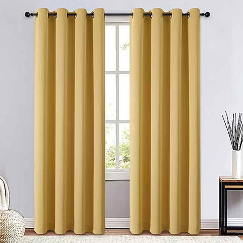Yellow blackout curtains with metal grommets, hung on a curtain rod, set in a minimalistic room with a light-colored wall, rug, and decorative items.
