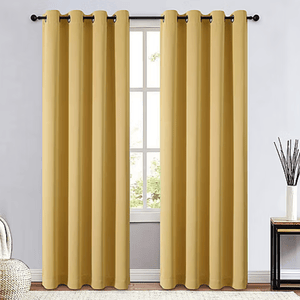 Yellow blackout curtains with metal grommets, hung on a curtain rod, set in a minimalistic room with a light-colored wall, rug, and decorative items.