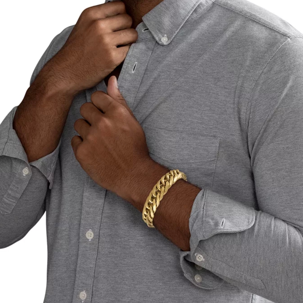 A man wearing a thick gold chain bracelet on his wrist while adjusting a button-up gray shirt.