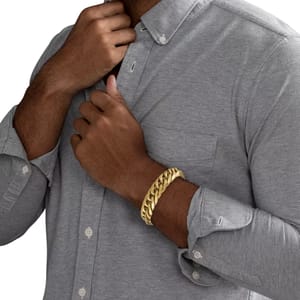 A man wearing a thick gold chain bracelet on his wrist while adjusting a button-up gray shirt.