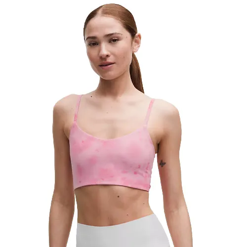 A woman is wearing a pink tie-dye cropped sports bra with thin straps and light-colored leggings.