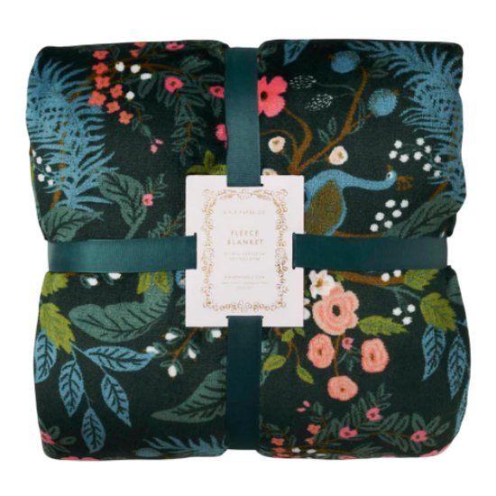 A folded fleece blanket features a dark background with a colorful floral and botanical pattern, including various flowers and leaves, held together by a dark green ribbon.