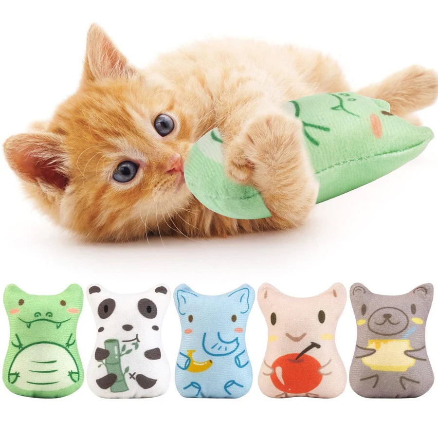 A ginger kitten plays with a green plush toy, part of a set featuring five animal-themed designs, including a crocodile, panda, elephant, apple, and bear. These toys are likely used for cat entertainment.