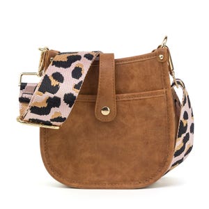 Brown faux-leather crossbody bag with a decorative button and a detachable, wide strap featuring a leopard print pattern in pink, black, and tan. Gold-tone hardware completes the design.