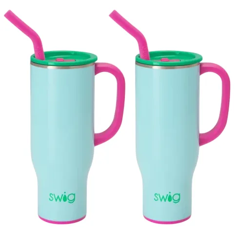 Two light blue insulated mugs with pink handles, green lids, and pink straws. The brand name \“swig\“ appears on each mug.