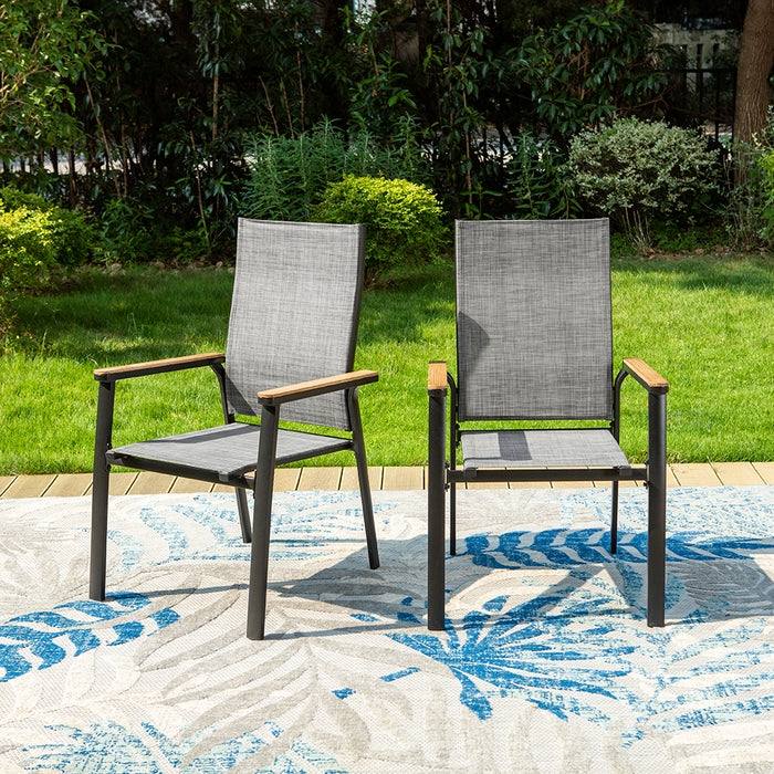Two modern outdoor chairs with gray mesh fabric and wooden armrests are placed on a patterned rug, set against a green lawn and lush garden background.